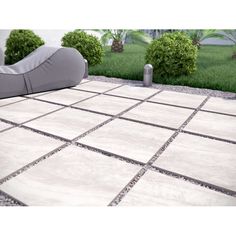 an outdoor area with white tiles and grey cushions on the ground, surrounded by green bushes