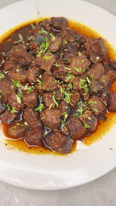 a white plate topped with meat covered in sauce and garnished with parsley