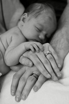 a black and white photo of a baby sleeping with his parents hands on it's chest