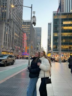 two people standing next to each other on a city street with tall buildings in the background