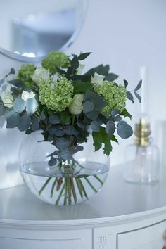 a vase filled with green flowers on top of a white table next to a mirror