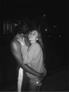 black and white photograph of two people embracing each other on the street at night time