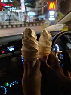 two ice cream cones are being held up in the car