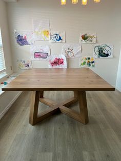 a wooden table sitting in the middle of a room with paintings on the wall behind it