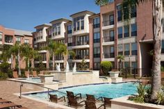 an outdoor swimming pool with lounge chairs and palm trees in front of the apartment buildings