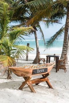 a wooden boat on the beach with palm trees in the foreground and a sign that says beer