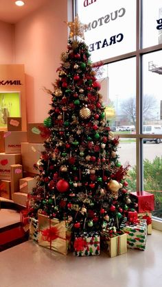 a decorated christmas tree sitting in front of a window next to boxes filled with presents