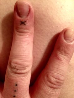 a woman's hand with a small cross tattoo on her thumb and ring finger