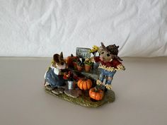 a figurine of two rabbits sitting on a bench with pumpkins and flowers