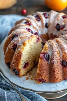 a bundt cake with icing and cranberries on a plate next to oranges