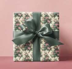 a wrapped present with a green bow on it's side and pink flowers in the background