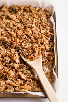 a pan filled with granola on top of a white table next to a wooden spoon