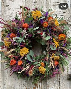 a wreath is hanging on the side of a door with flowers and leaves around it