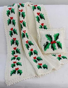 a white crocheted blanket with holly decorations on it and two matching pillow cases