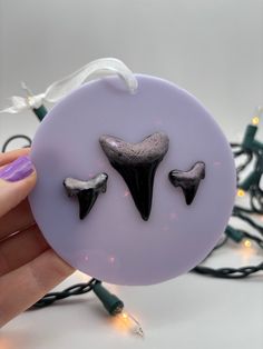 a hand holding a purple button with two black horns on it's face and string lights in the background