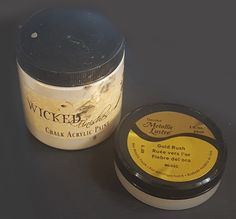 a jar of wax sitting next to a container of paste on a black table top