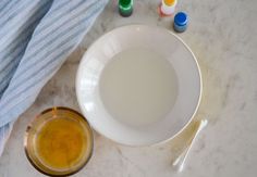 a white bowl with yellow liquid in it next to some markers and spoons on a marble surface