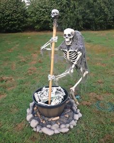 a skeleton statue holding a broom in a pot filled with rocks on the grass next to a fire pit