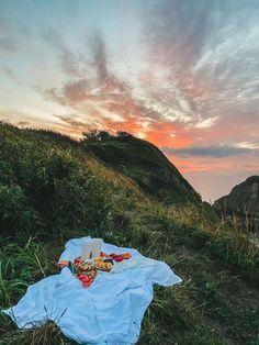 there is a blanket and food on the ground in front of a mountain at sunset