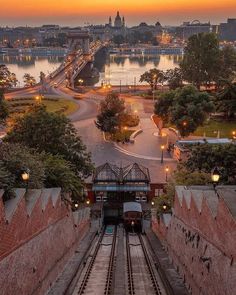 a train traveling down tracks next to a large body of water at sunset with buildings in the background