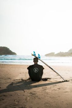 a man sitting on top of a sandy beach next to the ocean holding a surfboard