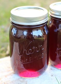 two jars filled with red liquid sitting on top of a wooden table next to grass