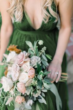 a woman in a green dress holding a bridal bouquet with flowers and greenery