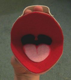 a hand holding a red felt heart with two black eyes and a white tongue on it