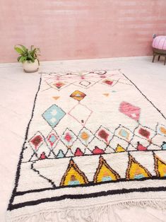 a white rug with multicolored designs on it in front of a pink wall