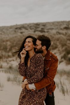 a man and woman are standing in the sand with their arms around each other as they laugh