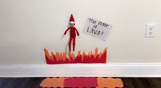 there is a paper cut out of an elf sitting on the floor next to a sign