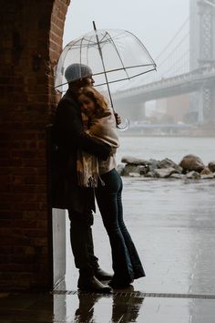 two people hugging under an umbrella on a rainy day in front of the brooklyn bridge