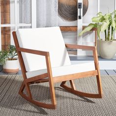 a white rocking chair sitting on top of a rug next to a potted plant