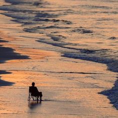 a person sitting in a chair on the beach watching the sun rise over the ocean