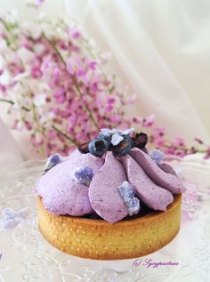 there is a purple cake with blueberries on it and flowers in the back ground