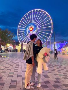 two people standing next to each other with a ferris wheel in the background at night