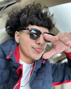 a young man wearing sunglasses sitting in the back seat of a car holding his hand up to his eye