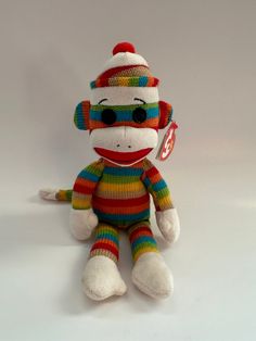 a sock monkey stuffed animal wearing a colorful hat and striped sweater sitting on a white surface