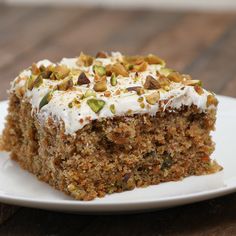 a piece of carrot cake on a plate with white frosting and pistachios