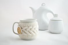 two coffee mugs and a teapot on a white background with one being knitted