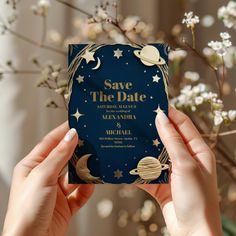 two hands holding up a wedding card with space and stars printed on it, in front of some flowers