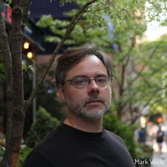 a man with glasses standing in front of a tree