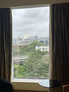 a window with curtains and a table in front of it, overlooking a cityscape