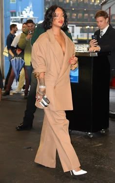 a woman walking down the street in a tan suit and white shoes with her hand on her hip