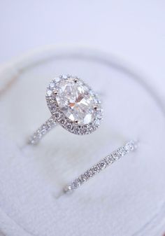 an oval diamond ring sits on top of a white cloth covered display case with two matching bands