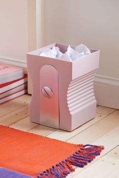 a pink tissue dispenser sitting on top of a wooden floor next to books