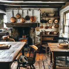 an old fashioned kitchen with wooden tables and chairs in front of a fire place that has pans hanging on the wall