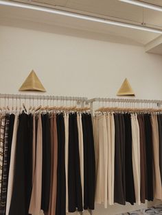 clothes hanging on racks in a room with white walls and flooring, two gold lamps above them