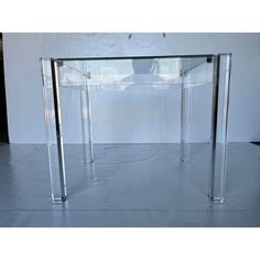 a clear glass table with metal legs in front of a white wall and black floor