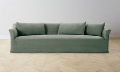 a green couch sitting on top of a hard wood floor next to a white wall